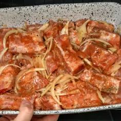 Babcine żeberka w sosie własnym, gotowe do pieczenia. Mięso w marynacie z cebulą i przyprawami w naczyniu żaroodpornym.