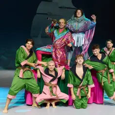 Aktorzy w barwnych strojach na scenie, przygotowujący się do spektaklu "Akademia Pana Kleksa teatr".