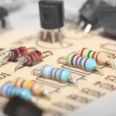 Na płytce drukowanej widoczne są elementy elektroniczne, w tym kolorowe rezystory i dioda zenera.
