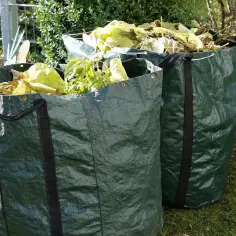 Dwa zielone worki na odpady ogrodowe wypełnione liśćmi i gałęziami.