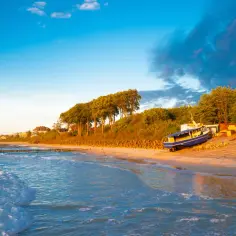Piękny zachód słońca nad Bałtykiem. Gdzie leży ustronie? Na piaszczystej plaży z łodzią i domkami w tle.