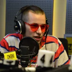 W studiu radiowym siedzi raper, który odpowiada na pytanie: jak ma na imię Żabson? Ma na sobie słuchawki i okulary.
