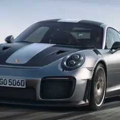 Srebrny Porsche GT2 RS z czarnymi pasami na masce i dachu pędzi po torze wyścigowym.