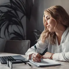 Kobieta pisze w notatniku, zastanawiając się, czy świadectwo pracy można wystawić wcześniej. Obok laptop i okulary.