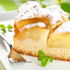 Pyszne, mega szybkie ciasto na oleju z jabłkami, posypane cukrem pudrem, na białym talerzu z miętą i widelcem.