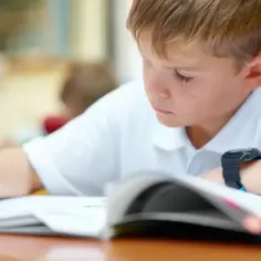Chłopiec w białej koszulce pisze w zeszycie, skupiony na zadaniu. To ważny etap jego edukacji, być może przygotowanie do rekrutacji.