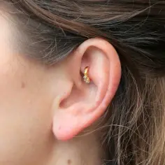 Złoty kolczyk w uchu, ozdobiony cyrkoniami, idealnie podkreśla urokliwy rook piercing.