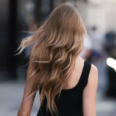 Kobieta z falującymi, blond włosami po perfekcyjnym blowout, idzie ulicą.