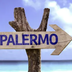Drewniany drogowskaz "PALERMO" na tle błękitnego nieba i morza. Czas zacząć planować, ile się leci do Palermo!