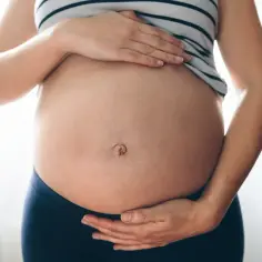 Ciąża to piękny czas, ale czasem pojawia się ból w okolicy pępka. Kobieta trzyma dłonie na brzuchu, ukazując jego zaokrąglenie.