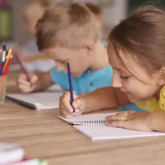 Dzieci skupione na nauce, rysują kredkami. To przykład kształcenia zintegrowanego, gdzie różne formy aktywności łączą się w procesie edukacyjnym.