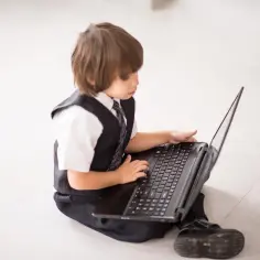 Chłopiec w garniturze próbuje dowiedzieć się, jak wyłączyć kontrolę rodzicielską na laptopie.