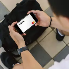 Osoba trzyma smartfon z logo mBank i kartą Mastercard.