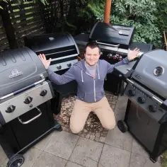 Mężczyzna klęczy otoczony kilkoma grillami gazowymi.