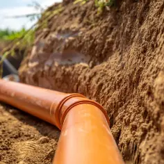 Pomarańczowa rura kanalizacyjna w wykopie. Może być podstawą do ubiegania się o odszkodowanie za studzienki na działce.