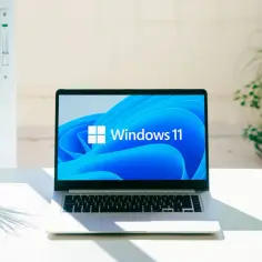 Laptop z systemem Windows 11 25H2 na biurku, obok doniczki z rośliną.