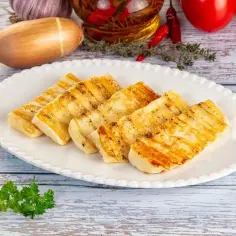 Grillowany serek halloumi na białym talerzu, z dodatkami: czosnkiem, cebulą, pomidorami i chili.