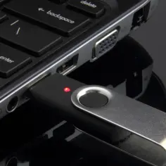 Pendrive podłączony do laptopa, gotowy do kopiowania zdjęć. Czerwona dioda sygnalizuje pracę.