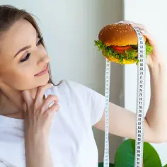 Kobieta z centymetrem krawieckim mierzy burgera, zastanawiając się, ile kalorii dziennie powinna spożywać.