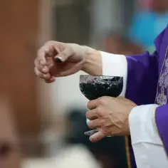 Kapłan w fioletowej szacie trzyma kielich z winem. To ważny moment podczas mszy, wypełniający święta nakazane.