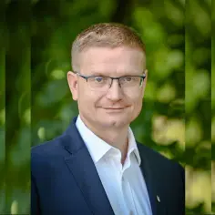 Krzysztof Matyjaszczyk, prezydent Częstochowy, w granatowej marynarce i białej koszuli, na tle zieleni.