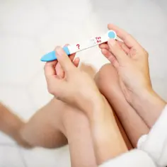 Kobieta trzyma test ciążowy z pytajnikiem. Czy w połogu można zajść w ciążę? Wynik nie jest jeszcze widoczny.