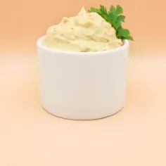 Puszysty hummus z ciecierzycy, udekorowany gałązką natki pietruszki, w białej miseczce.
