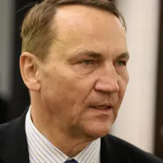 Minister spraw zagranicznych w garniturze i pasiastym krawacie, z uwagą wpatrujący się w dal.