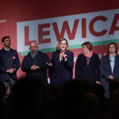 Grupa osób stoi na scenie przed napisem "LEWICA". Kobieta w środku mówi do mikrofonu.