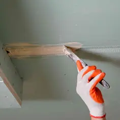 Ręka w rękawicy nakłada masę szpachlową na połączenie płyt gipsowych, przygotowując je do dalszych prac.