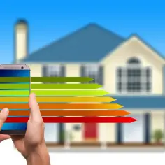 Porównanie efektywności energetycznej: pompa ciepła czy pellet? Smartfon pokazuje wykres, dom w tle.