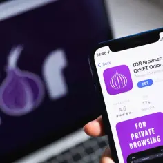 Telefon z aplikacją przeglądarka tor. Na ekranie laptopa widnieje logo Tor.