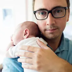 Ojciec z okularami tuli śpiące dziecko. Czy na urodzenie dziecka należy się urlop okolicznościowy?