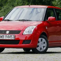 Czerwony Suzuki Swift, idealne auto do 20 tys. zł, z tablicą WB 94453, zaparkowany na zewnątrz.