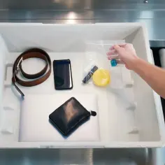 Na lotniskowej taśmie widać przedmioty do kontroli: pasek, telefon, portfel, laptop i przezroczystą torebkę z płynami. Taką butelkę można wziąć do samolotu.