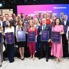 Grupa osób w garniturach i sukienkach trzyma dyplomy na tle ekranu z napisem "XIX Ranking Firm Doradztwa Podatkowego".