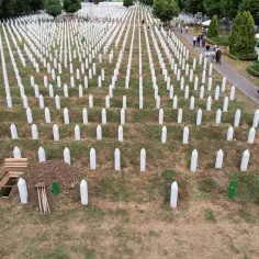 Cmentarz w Srebrenicy, rzędy białych nagrobków upamiętniają ofiary ludobójstwa. Widać świeżo wykopany grób.