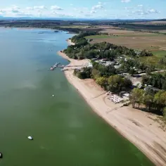 Piękna, piaszczysta mietków plaża z łódkami na zielonej wodzie i lasem w tle.