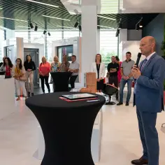 Mężczyzna w garniturze przemawia do grupy ludzi w nowoczesnym salonie okien i drzwi.