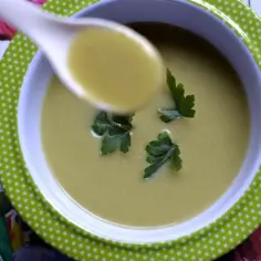 A spoonful of creamy zupa krem z brokułów z ziemniakami, garnished with parsley, sits in a green polka-dot bowl on a floral background.