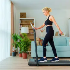 Kobieta w sportowym stroju ćwiczy na bieżni w domowym salonie.