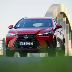 Czerwony suv Lexus NX z charakterystycznym grillem i ostrymi światłami stoi na tle łukowatego mostu.