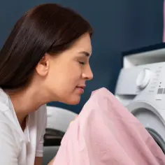 Kobieta wącha różowy materiał, szukając prawdziwych powodów dla których pranie śmierdzi stęchlizną po wyjęciu z bębna.