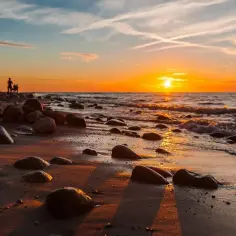 Zachód słońca w Jarosławcu. Kamienista plaża, fale obmywają brzeg, a na horyzoncie złote słońce.