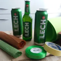 Materiały do stworzenia prezentu z piwa: puszki i butelka Lecha, kolorowe papiery, wstążka i taśma.