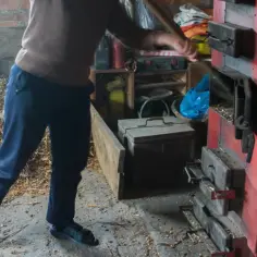 Osoba wsypuje materiał do czerwonego pieca na pellet.