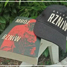 Książka "Mróz RZNiW" i czapka z napisem "Osiedle RZNiW" na tle zieleni.