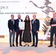 Pięć osób w garniturach i sukience pozuje do zdjęcia z dyplomem na tle grafiki z wagą sprawiedliwości.