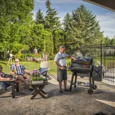Rodzina cieszy się latem przy grillu z wędzarnią. Dzieci bawią się na trawniku, a dorośli relaksują się z napojami.