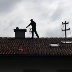 Cień kominiarza na dachu, który przygotowuje się do czyszczenia komina, by jak wypalić sadzę.